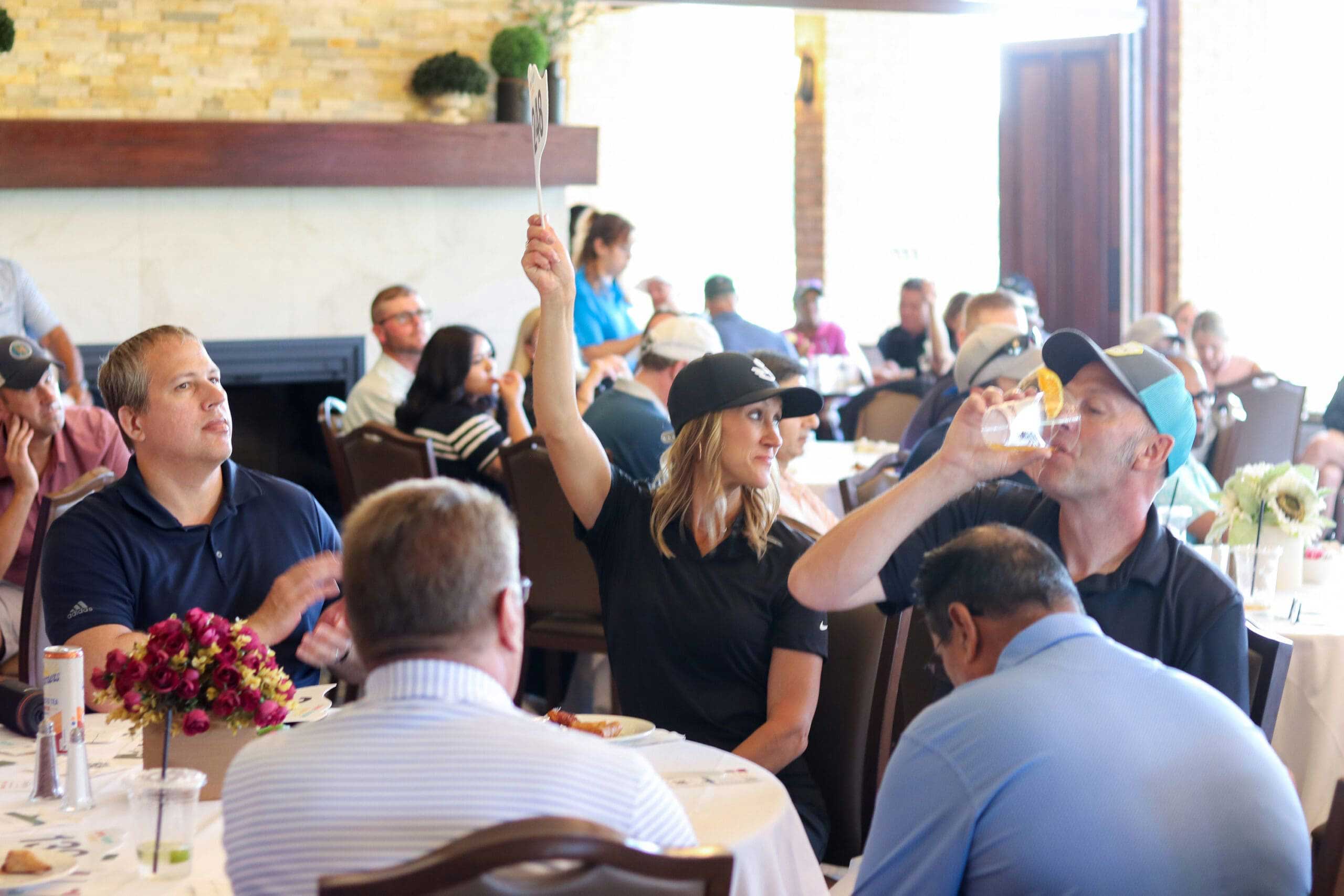 A woman raises her paddle to donate during the paddle raise at One Hope United's Charity Golf Outing.