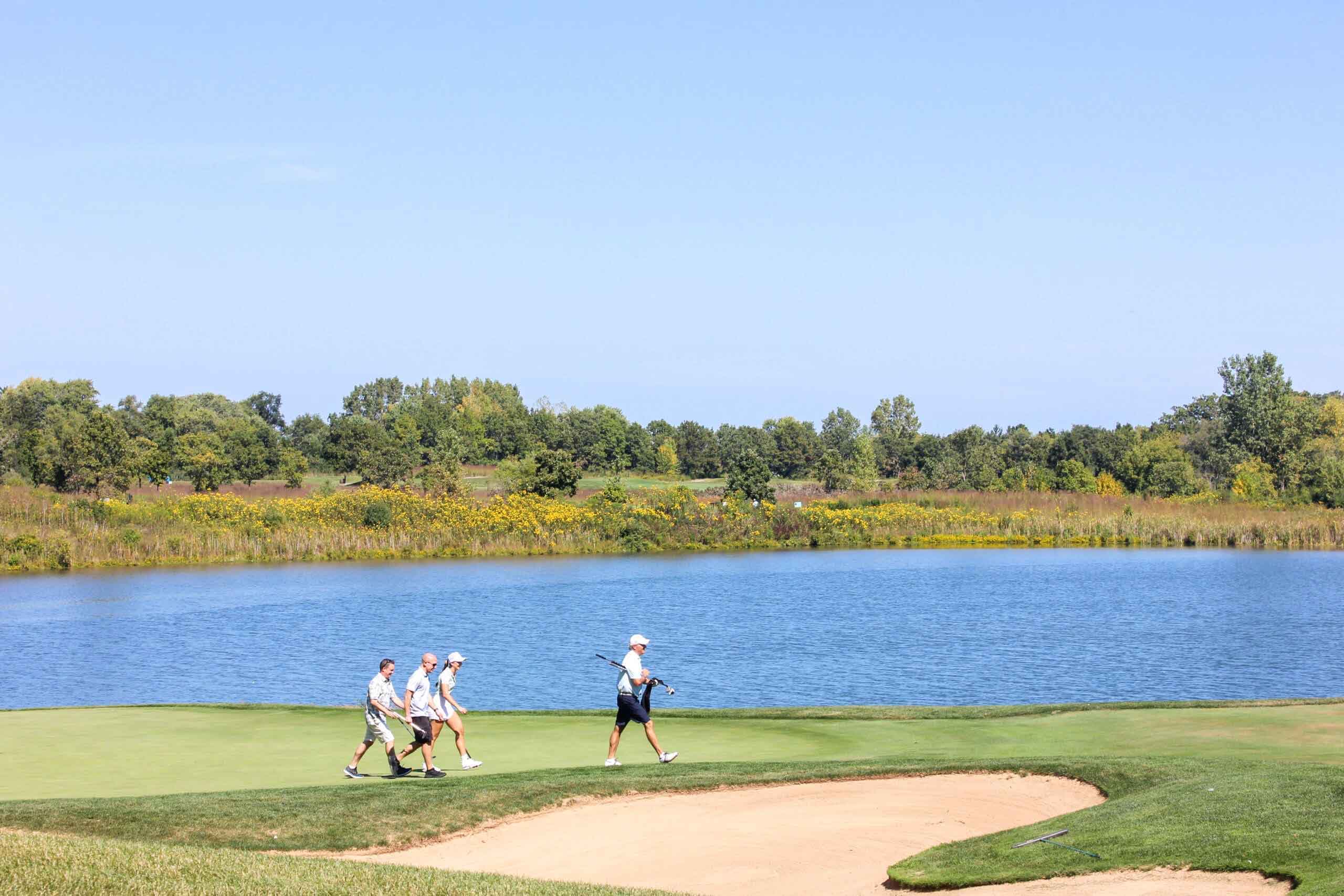 Golfers walk across the green in front of a body of water at One Hope United's Charity Golf Outing.