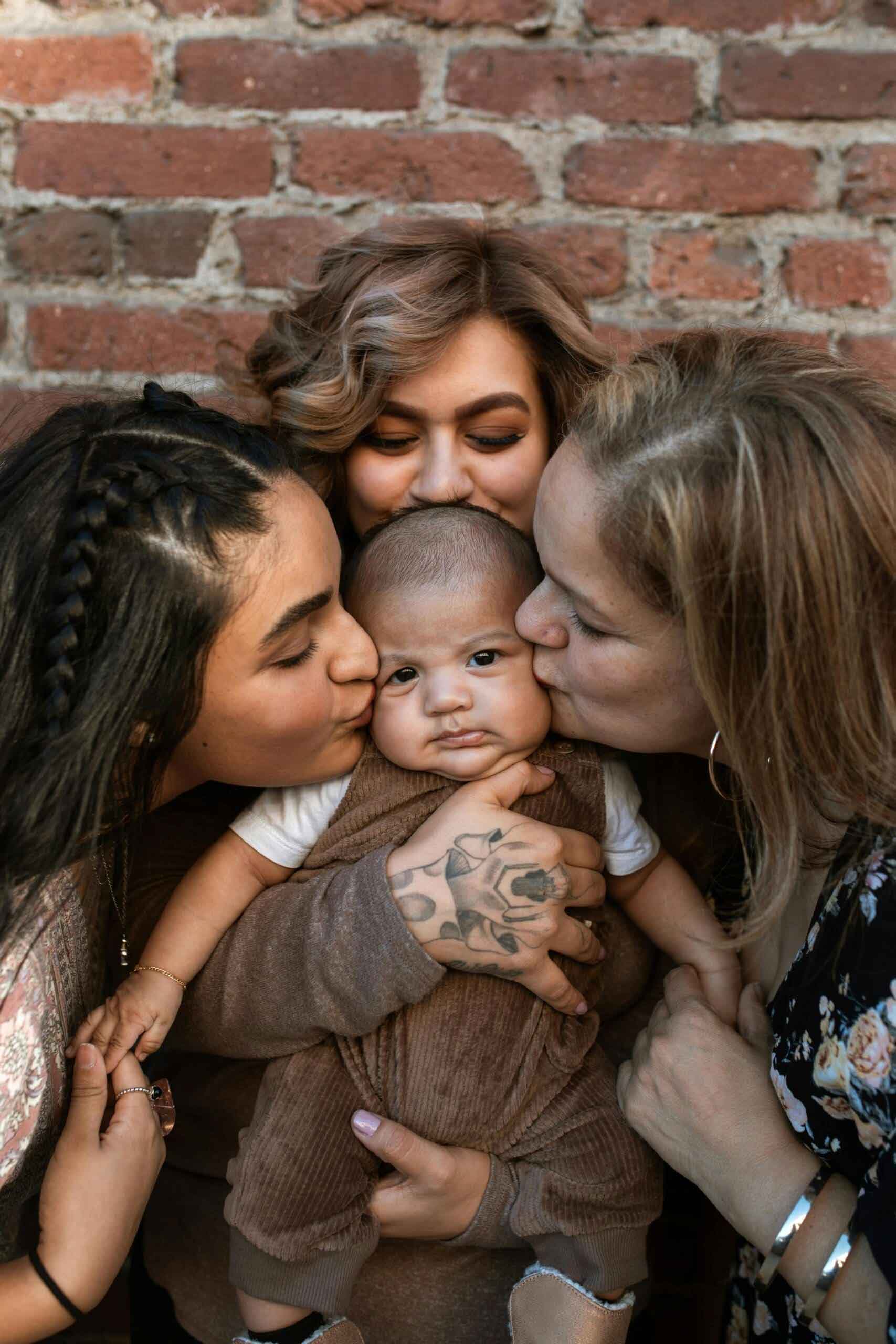 Three women lovingly embrace a baby, exemplifying family warmth and connection.